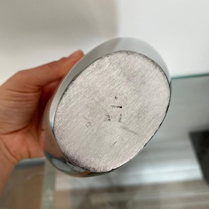 Pu&ograve; includere: Una fiaschetta color argento di forma ovale. Il fondo della fiaschetta presenta dei segni incisi. La fiaschetta &egrave; tenuta da una persona.