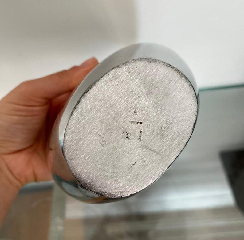 Pu&ograve; includere: Una fiaschetta color argento di forma ovale. Il fondo della fiaschetta presenta dei segni incisi. La fiaschetta &egrave; tenuta da una persona.