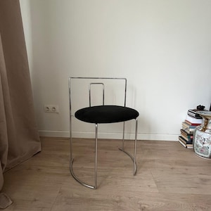 May include: A modern chair with a black circular seat and a chrome-colored metal frame. The chair has a curved base and a rectangular backrest. The design is minimalist and suitable for various interior styles.