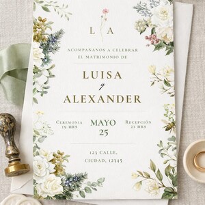 May include: A white wedding invitation card featuring gold text and a botanical border of white roses, green leaves, and berries. The text reads ACOMPAÑANOS A CELEBRAR EL MATRIMONIO DE LUISA y ALEXANDER, CEREMONIA 19 HRS, MAYO 25, RECEPCIÓN 21 HRS, 123 CALLE, CIUDAD, 12345.