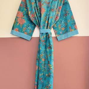 May include: A long-length robe in a vibrant teal blue featuring a colorful floral and bird print. The garment includes wide sleeves with white and blue striped cuffs, a matching tie belt at the waist, and a coordinating striped collar trim.