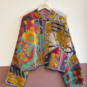 May include: A cropped jacket made from quilted fabric featuring a patchwork of various floral and geometric patterns in shades of yellow, red, teal, and black. The garment has long sleeves, a mandarin collar, and black and white striped trim.