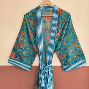 May include: A teal kimono-style robe featuring a vibrant floral and bird print in shades of orange, pink, and green. The garment includes white and blue vertical striped trim along the front opening, sleeve cuffs, and the matching waist tie belt.
