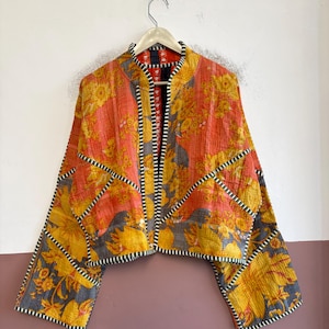 May include: A cropped jacket featuring a vibrant orange and yellow floral pattern with grey accents. The garment has a mandarin collar, wide sleeves, and black and white striped trim along the edges, all constructed with visible quilted stitching.