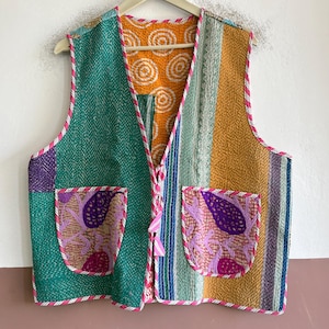 May include: A sleeveless waistcoat featuring a patchwork design with quilted fabric in shades of green, yellow, and orange. The garment includes two front pockets with purple and pink floral patterns, finished with a pink and white striped trim.