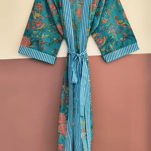 May include: A teal kimono robe featuring a vibrant floral and bird print in shades of orange, yellow, and green. The garment includes a white and teal vertical striped trim along the front opening, sleeve cuffs, and a matching tie-waist belt.