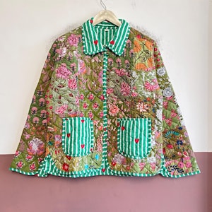 Pode incluir: Um casaco acolchoado com um padrão floral verde estampado em blocos e acabamentos às riscas brancas e verdes no colarinho, punhos e bolsos. A peça inclui pequenos bordados de corações vermelhos como detalhe no colarinho e nos bolsos.