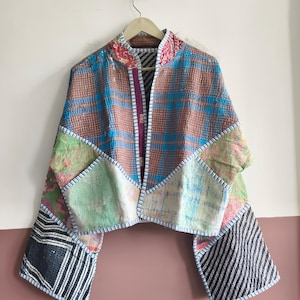 May include: A cropped jacket constructed from patchwork fabric featuring a variety of patterns including brown and blue plaid, light green floral, and black and white stripes. The garment has long sleeves, an open front, and visible stitching.