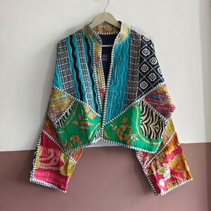以下が含まれることがあります： ターコイズ、グリーン、イエロー、ピンク、ブラックの色合いで、花柄、幾何学模様、ストライプなど、さまざまなカラフルなパターンをパッチワークしたキルティング生地のクロップドジャケット。スタンドカラーと長袖が特徴です。