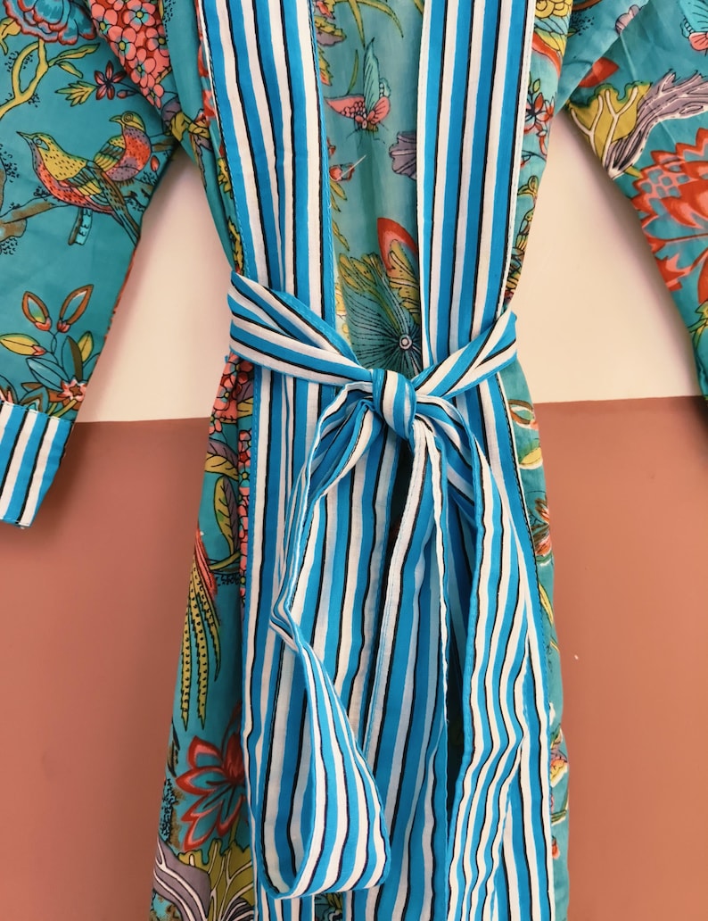May include: A turquoise robe featuring a vibrant floral and bird pattern in shades of pink, yellow, and green. The garment includes a wide front placket and a matching tie belt, both decorated with vertical white, navy blue, and light blue stripes.
