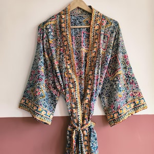 May include: A long-sleeved robe featuring a dark teal base with an intricate, multicolored floral and geometric pattern in shades of yellow, pink, and white. The garment includes a matching tie belt and a wide, contrasting border along the front opening.