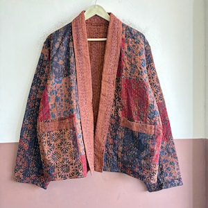 Könnte beinhalten: Eine langärmelige Jacke mit Patchwork-Design, bestehend aus verschiedenen Blumen- und geometrischen Mustern in Marineblau, Rostorange und Dunkelrot. Das Kleidungsstück hat einen einfarbigen rostfarbenen Kragen, eine offene Vorderseite und zwei aufgesetzte Taschen.