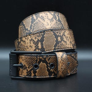 May include: A belt featuring a brown and black snakeskin pattern with a matte black buckle and hardware. The buckle is embossed with the text LOWLIFE. The belt strap is coiled, showing the textured reptilian print across the entire surface.