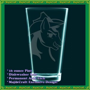 May include: A 16 ounce glass pint with a design etched into the side. The design is a gray silhouette of a unicorn's head with a horn and a hat. The text on the glass reads "16 ounce Pint", "Dishwasher Safe", "Permanent Acid Etch", and "MajikCraft Exclusive Design."