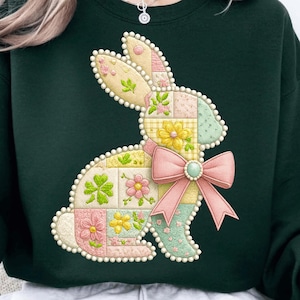 May include: Dark green sweatshirt with a patchwork bunny design. The bunny is made of pastel squares with floral and clover patterns. A pink bow with a green gem is on the bunny's neck. The design has a dotted border.