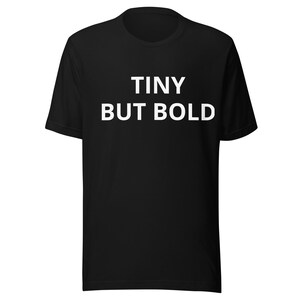 Puede incluir: Camiseta negra con el texto blanco "TINY BUT BOLD" en el pecho. La camiseta tiene mangas cortas y cuello redondo. La tela parece suave y cómoda.