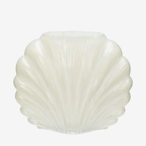 Puede incluir: Un jarrón decorativo con forma de concha, de color blanco nacarado. El jarrón tiene un borde festoneado y una superficie texturizada, imitando la forma de una concha real. El diseño es elegante y adecuado para la decoración de temática costera.