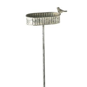 Può includere: Una vasca per uccelli in metallo zincato su un paletto. Il bacino ovale ha un design strutturato e ondulato ed è sormontato da una piccola statuina di uccello. Il paletto è un palo sottile e dritto, perfetto per un giardino.