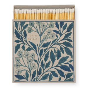 May include: A rectangular matchbox filled with wooden matches featuring white tips. The box exterior is light beige with a dark blue botanical pattern of leaves and small flowers. The text "luxury matches" is printed in gold on the front.