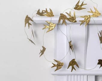 Puede incluir: Una guirnalda decorativa que presenta múltiples adornos de aves de color dorado metálico suspendidos en un alambre fino y flexible. Cada ave está formada con detalles en las alas y plumas de la cola, creando un patrón a lo largo del alambre.