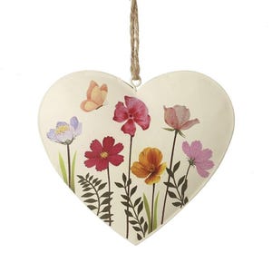 May include: Cream-colored heart-shaped metal wall hanging with a floral design. The artwork features colorful flowers in shades of red, pink, orange, and purple, along with a small orange butterfly. A natural twine loop is attached for hanging.