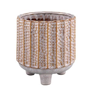 Peut inclure: Un pot de fleurs cylindrique en céramique présentant une surface texturée avec des bandes verticales de points beiges en relief et tachetés, alternant avec des rainures lisses et brunes. Le récipient repose sur trois pieds courts et gris.