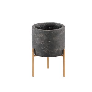 May include: A cylindrical dark grey planter with a textured, weathered surface finish. The planter is supported by a gold-toned metal stand featuring three thin, vertical legs that provide elevation and stability for the container.