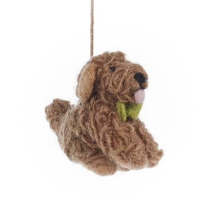May include: A brown, handmade dog ornament with a green bow tie and a pink tongue. The dog is made of a textured, woven material and is suspended by a natural twine string. The dog is in a sitting position.