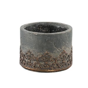 Peut inclure: Un pot de fleurs cylindrique en béton gris foncé avec une texture craquelée et vieillie. La base est entourée d'une garniture métallique ornementale en relief de couleur cuivre avec un motif répétitif de fleur de lys.