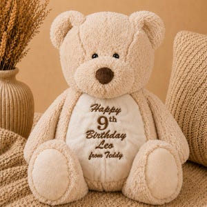 Könnte beinhalten: Ein beigefarbener Plüsch-Teddybär mit einer dunkelbraunen Nase und schwarzen Augen. Der Bär hat einen cremefarbenen Bauchfleck, der mit dem Text bestickt ist: Happy 9th Birthday Leo from Teddy. Der Text Personalised Zippie Teddy Bear Keepsake ist sichtbar.