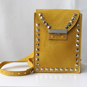 May include: A mustard yellow suede crossbody bag with silver pyramid studs around the edges and a silver clasp closure.