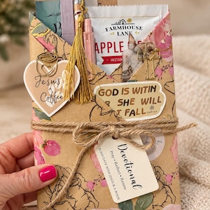 May include: A gift set wrapped in floral paper featuring a heart-shaped tag reading Jesus + Coffee, a gold tassel, a pencil, a Farmhouse Lane apple cider packet, a cross-shaped paperclip, and a sticker stating God is within her she will not fall.