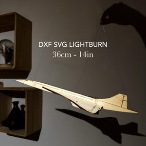 Puede incluir: Maqueta de madera de un avión Concorde, suspendida por cuerdas. El modelo mide 36 cm de largo y tiene cortes detallados. El texto "DXF SVG LIGHTBURN" y "36cm - 14in" se muestra en la imagen. El avión proyecta una sombra.