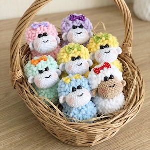 May include: A woven basket containing seven handmade crochet sheep toys. Each sheep has a different pastel-coloured wool, a white face, and a small bow. The sheep are in shades of pink, purple, yellow, green, blue, and white. A charming, handcrafted collection.