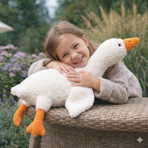 May include: A plush white goose with an orange beak and feet. The stuffed animal is made of a soft, textured material. The goose is being held by a smiling child.