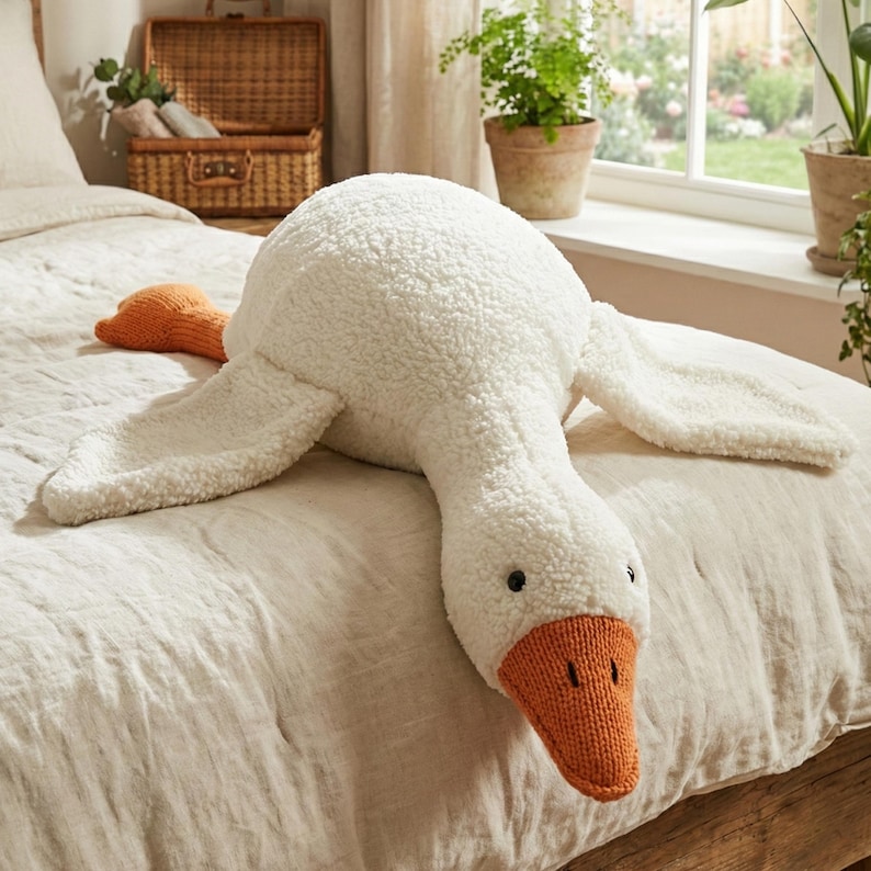 May include: A large, plush white goose-shaped pillow with an orange beak and feet rests on a bed. The pillow has a soft, textured surface and black button eyes. The wings are spread out, and the pillow is designed for comfort and decoration.