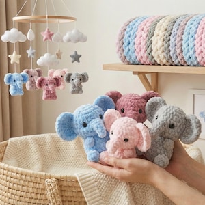 May include: A collection of handmade crochet elephants in various pastel colors, including blue, pink, and gray. Some elephants are displayed as a mobile with clouds and stars. The soft toys are displayed near a woven basket.