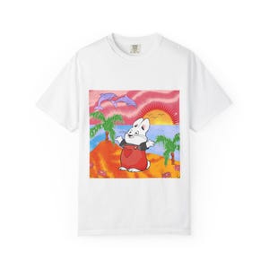 May include: White t-shirt featuring a cartoon illustration of a rabbit on a tropical island with palm trees, dolphins, and a sunset. The rabbit wears red overalls with a heart. A fun, colorful design for kids.