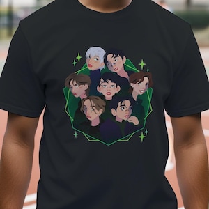 May include: Black t-shirt featuring a graphic of nine cartoon faces within a green geometric design. The faces have various hair colors and styles. The t-shirt is being worn on a basketball court.