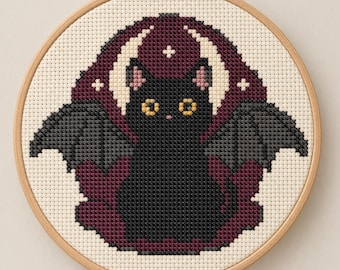 May include: A cross-stitch embroidery in a round wooden hoop featuring a black cat with bat wings. The cat has yellow eyes and pink inner ears, centred against a dark maroon circular background with a white crescent moon and small cross symbols.
