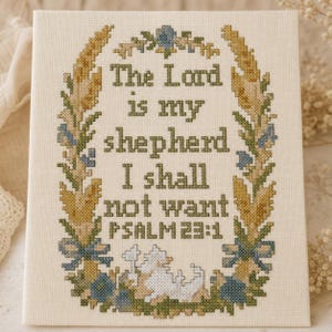 May include: A rectangular cross-stitch embroidery on off-white fabric featuring the text The Lord is my shepherd I shall not want PSALM 23:1 in dark green. The text is framed by a wreath of yellow wheat stalks, blue flowers, and green leaves.