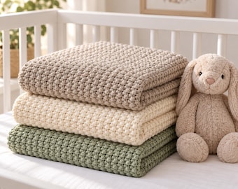 May include: A stack of three folded blankets with a textured bobble stitch pattern in beige, cream, and sage green, accompanied by a plush beige stuffed rabbit toy with long ears, all resting on a white surface within a white crib frame.