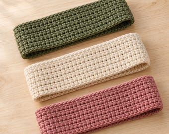 May include: Three rectangular headbands featuring a dense, textured crochet stitch pattern. The headbands are presented in a solid olive green, a creamy off-white, and a muted dusty rose colour, each displaying a consistent, uniform knit construction.