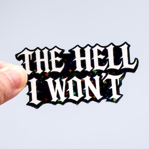 Op de afbeelding: Een holografische sticker met de tekst "THE HELL I WON'T" in een vet, gotisch lettertype. De sticker heeft een zwarte achtergrond met kleurrijke stervormige accenten en een witte rand.