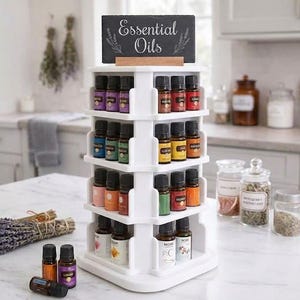 May include: A white, four-tiered rotating display stand holding numerous small glass essential oil bottles. A rectangular black sign with the white text "Essential Oils" sits on top. Three additional oil bottles lie on the surface in front.