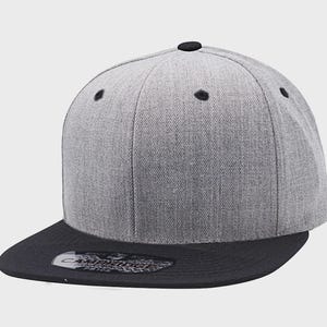 May include: A gray and black baseball cap with a flat brim. The cap features a gray crown with black ventilation eyelets and a black button on top. The brim is black, and the cap has a structured, modern design.