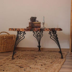 May include: A coffee table with a live edge wooden top and decorative black metal legs. The table is decorated with books, dried flowers, and a candle holder. A woven basket and rug create a natural, cosy atmosphere.