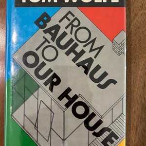May include: A hardcover book titled From Bauhaus to Our House by Tom Wolfe. The cover features a black rectangular header with white text, and a graphic illustration of a building structure in gray, blue, red, green, and yellow geometric shapes.