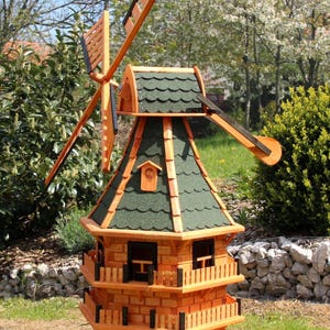 Puede incluir: Un modelo de molino de viento de madera con un tejado de tejas verdes y una estructura de madera marrón-naranja. El molino de viento tiene un diseño de varios niveles con balcones y un ventilador giratorio. El modelo está al aire libre en un jardín.