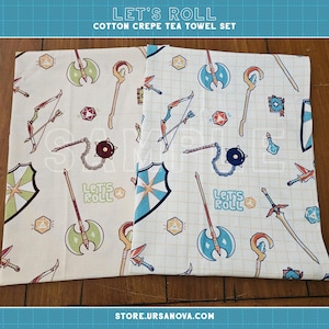 May include: Two cotton crepe tea towels with a repeating pattern of fantasy weapons and icons in blue, green, and red on a cream background. The text "LET'S ROLL" is printed on the towels.